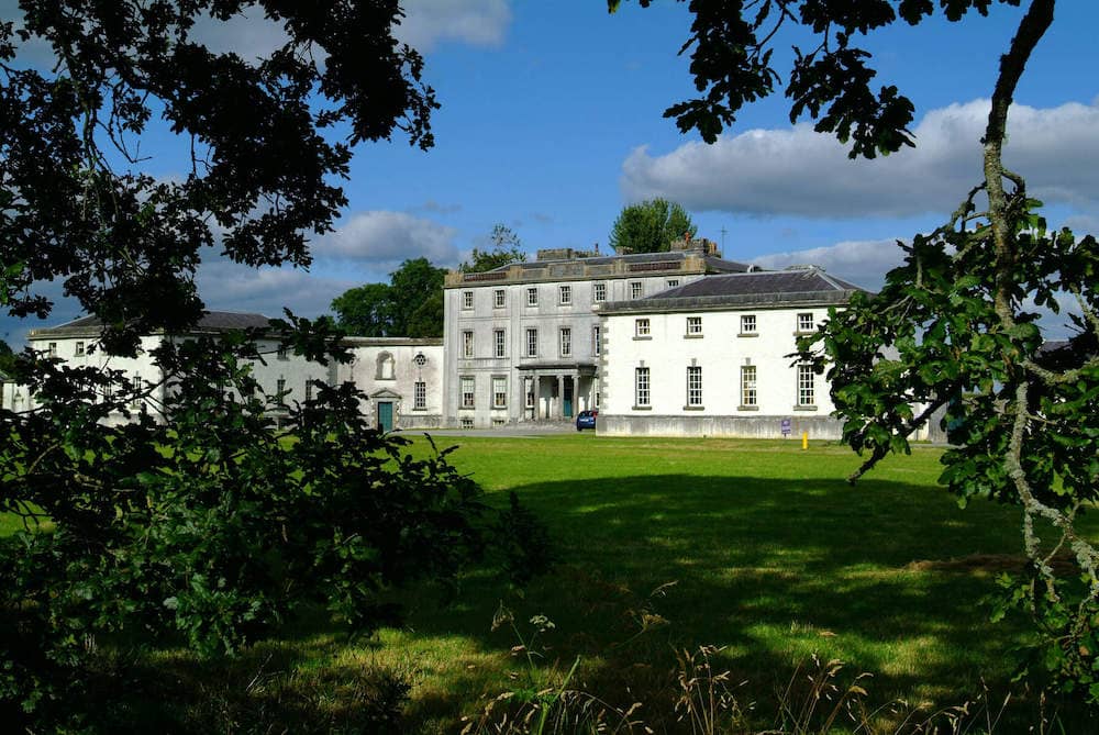 Strokestown Park House, a grand 18th-century estate framed by trees and set against a bright blue sky.
