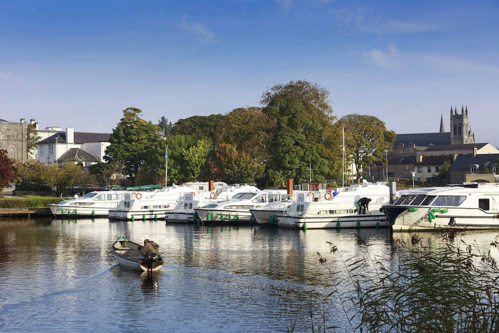 Boats docked in Carrick-on-Shannon marina with church spire and trees in the background.