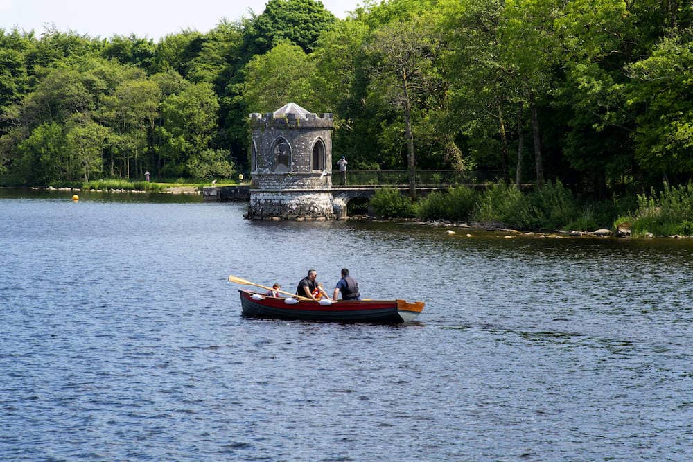A small boat rows past the turreted island folly on Lough Key, surrounded by lush forest.
