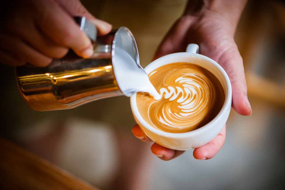Barista pouring steamed milk into a coffee cup to create leaf-pattern latte art in Armagh.