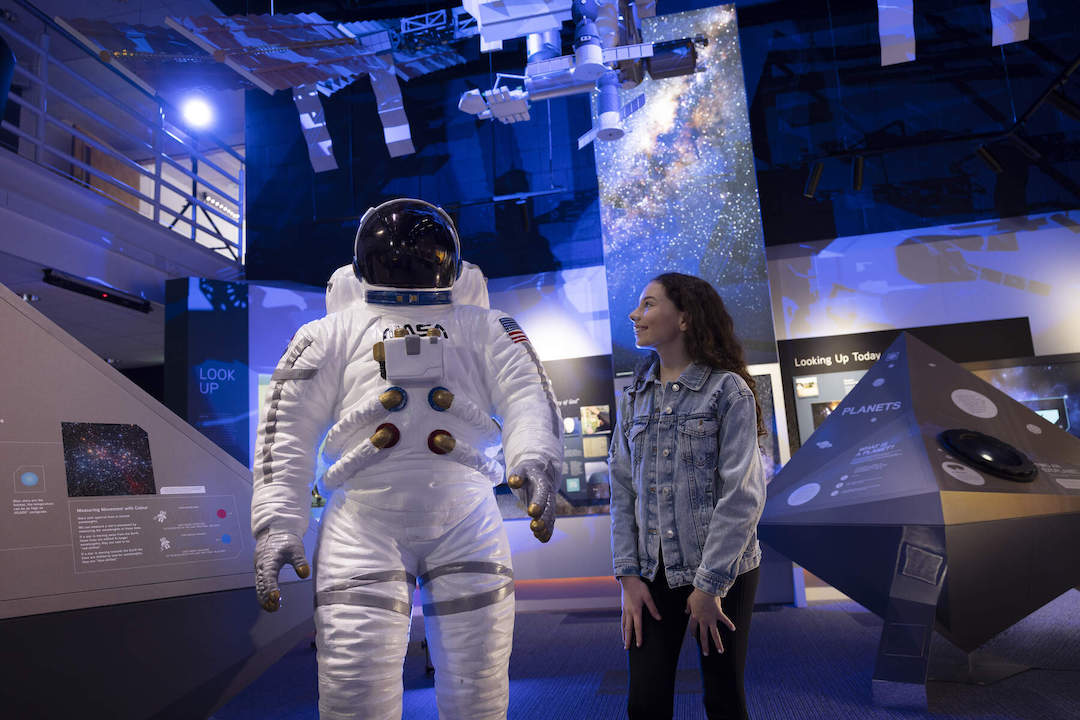Girl standing beside a NASA space suit replica at Armagh Planetarium’s interactive exhibition.