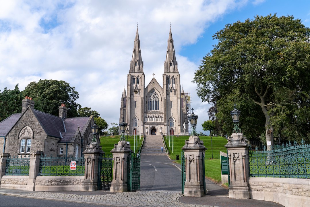 St Patrick’s Cathedral in Armagh seen from main gates with stone gatehouses and tree-lined path.