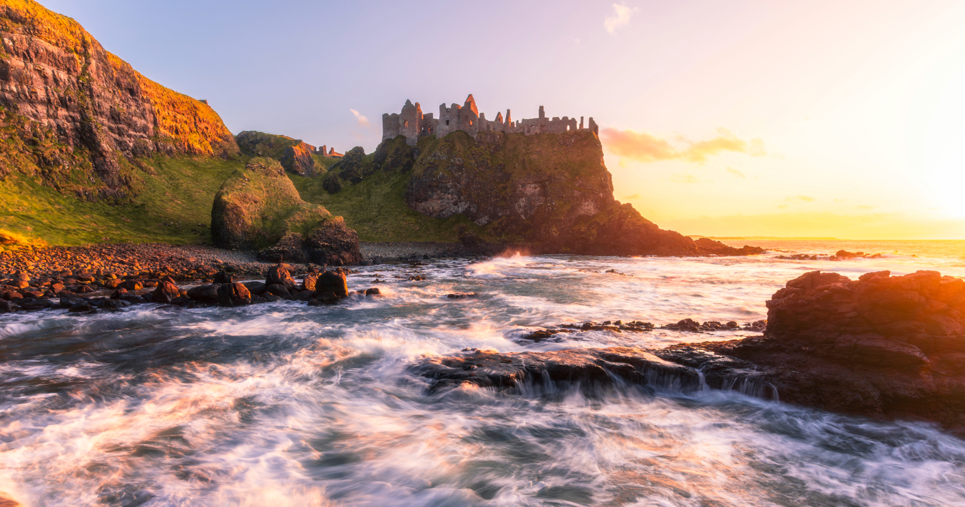 Dunluce Castle boven de beukende golven aan de Causeway kust bij zonsondergang, county Antrim.
