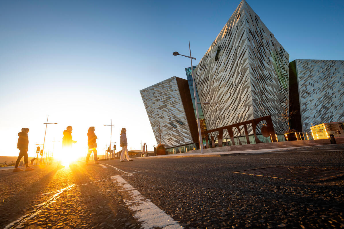 Mensen die bij zonsondergang langs Titanic Belfast lopen in het Titanic Quarter.