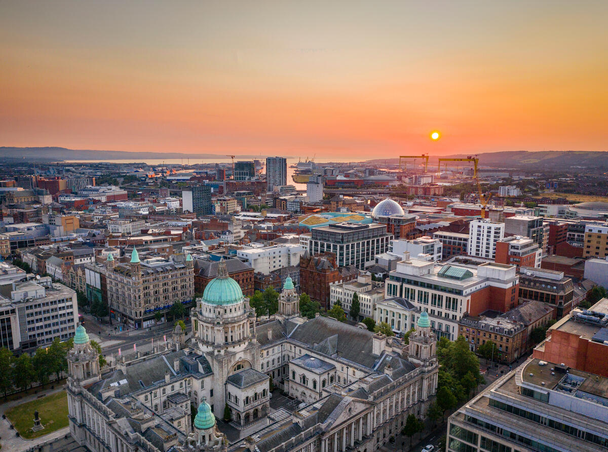 Luchtfoto van het stadhuis van Belfast en de skyline van de stad bij zonsondergang, met daarachter Belfast Lough.