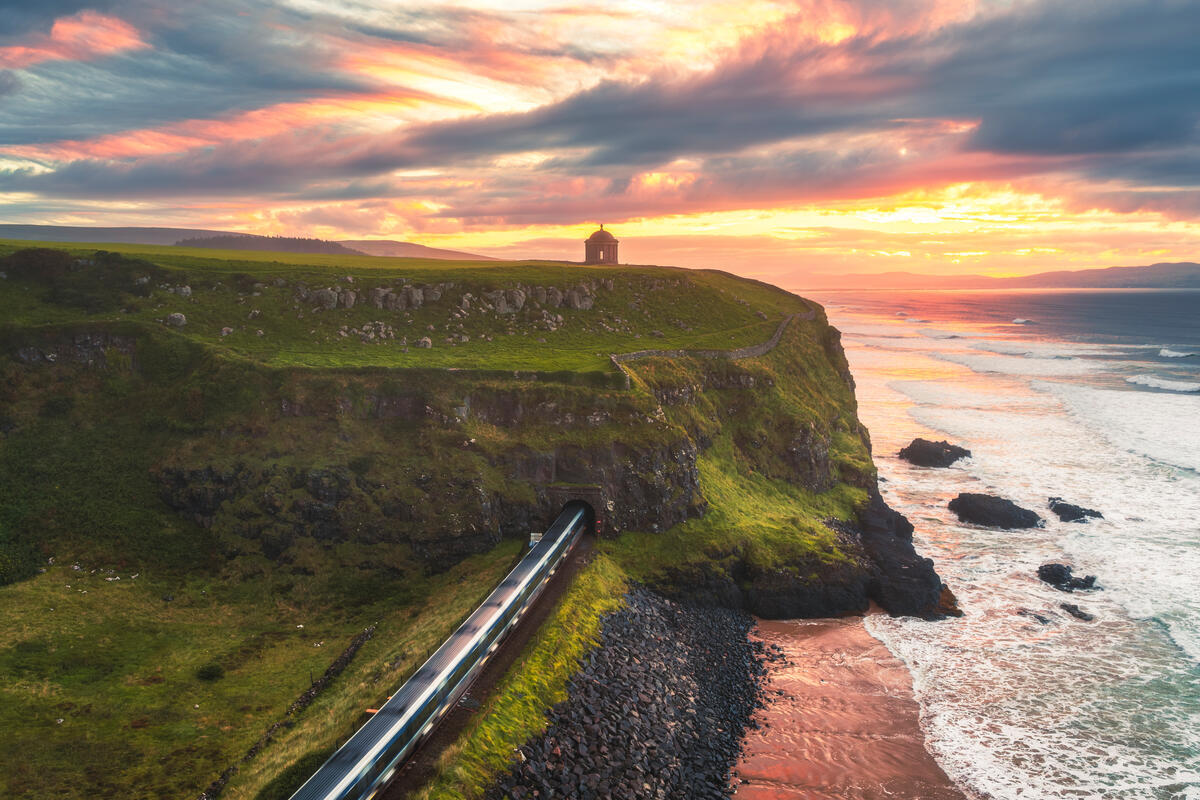 Een trein die bij zonsondergang onder de Mussenden Temple tevoorschijn komt, naast Downhill Strand, county Londonderry.