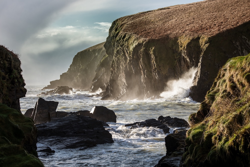 Waves crashing against rugged sea cliffs along the Wild Atlantic Way in County Cork.