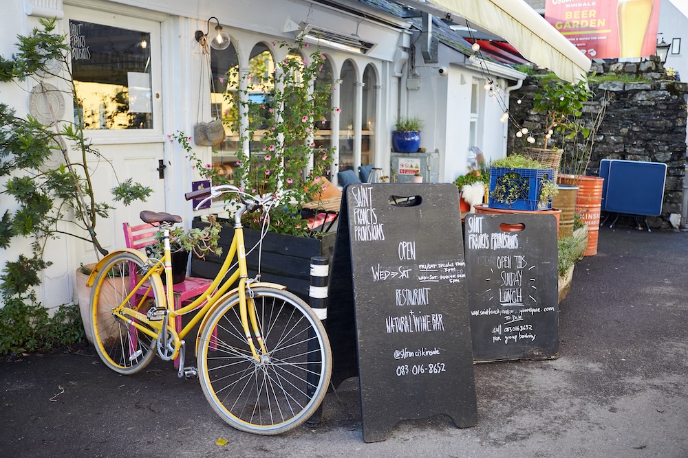 Yellow bicycle outside Saint Francis Provisions restaurant with chalkboard signs in Kinsale, County Cork.