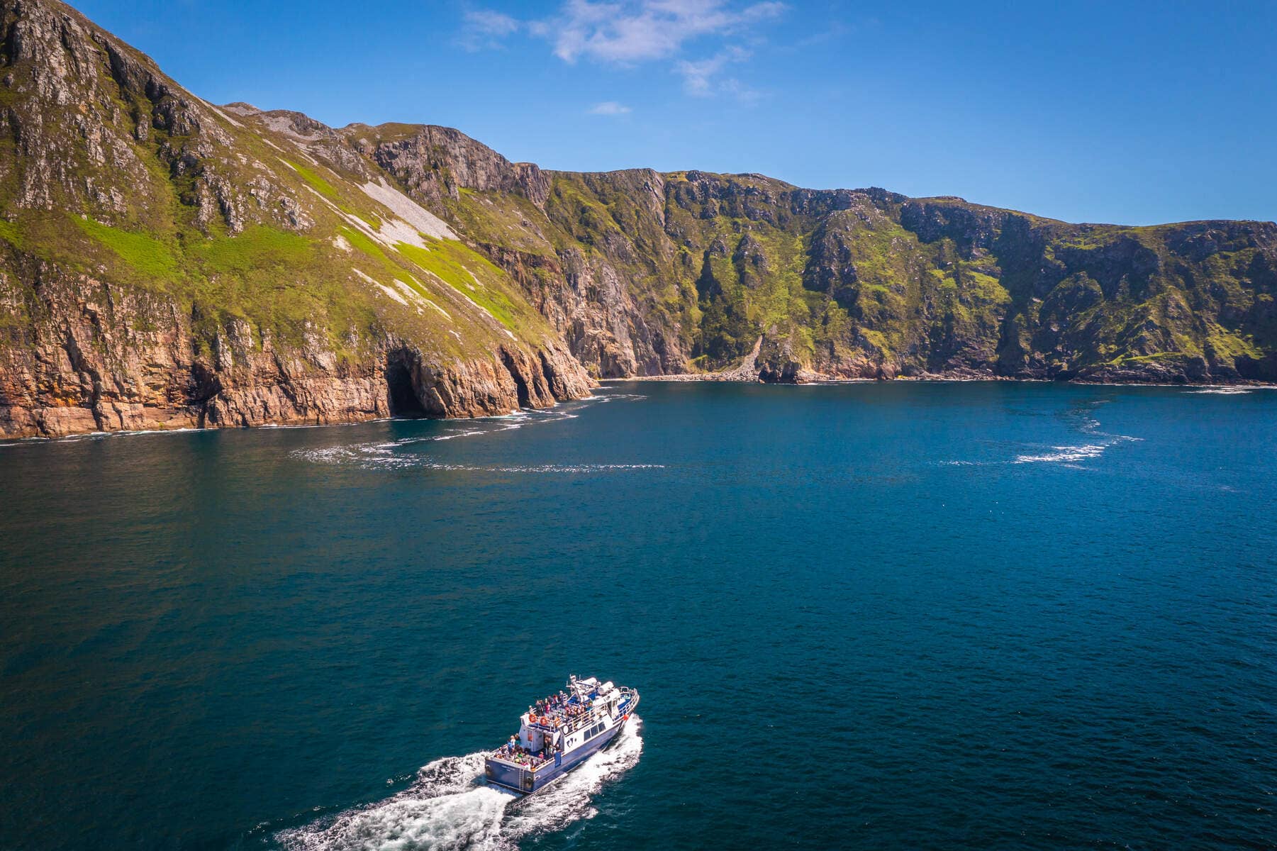 Rondvaartboot onder de torenhoge zeekliffen van Slieve League in county Donegal op een heldere zomerdag.