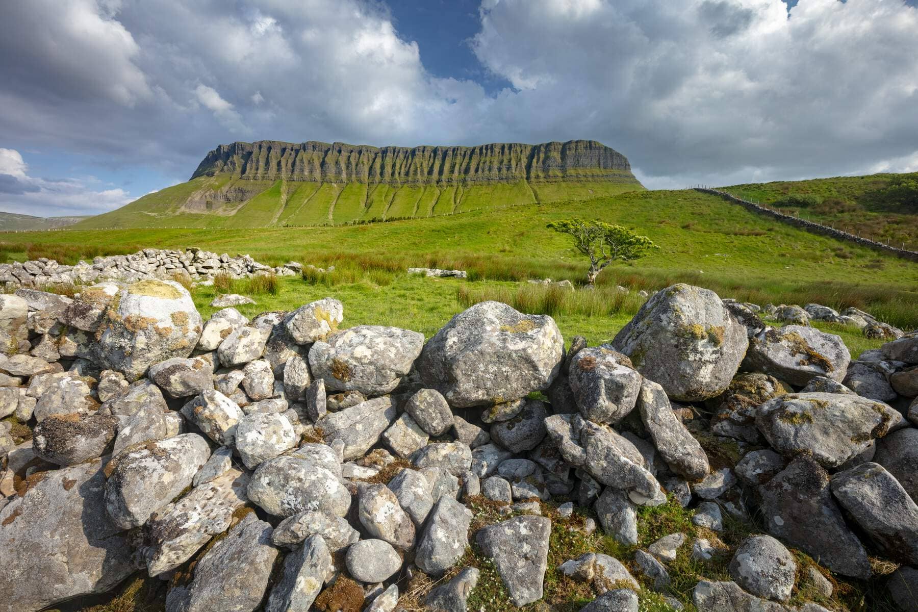 De berg Ben Bulben in county Sligo torent boven groene velden en een traditionele, droge stenen muur onder een prachtige lucht.