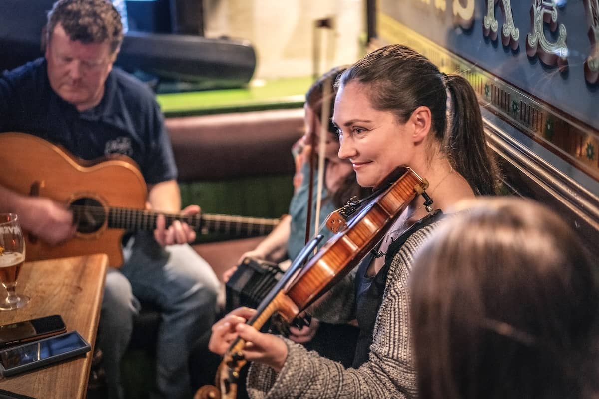 Traditionelle irische Musiksession im McHigh's Pub während des Belfast Tradfest mit Musikern, die in gemütlicher Atmosphäre Geige und Gitarre spielen.