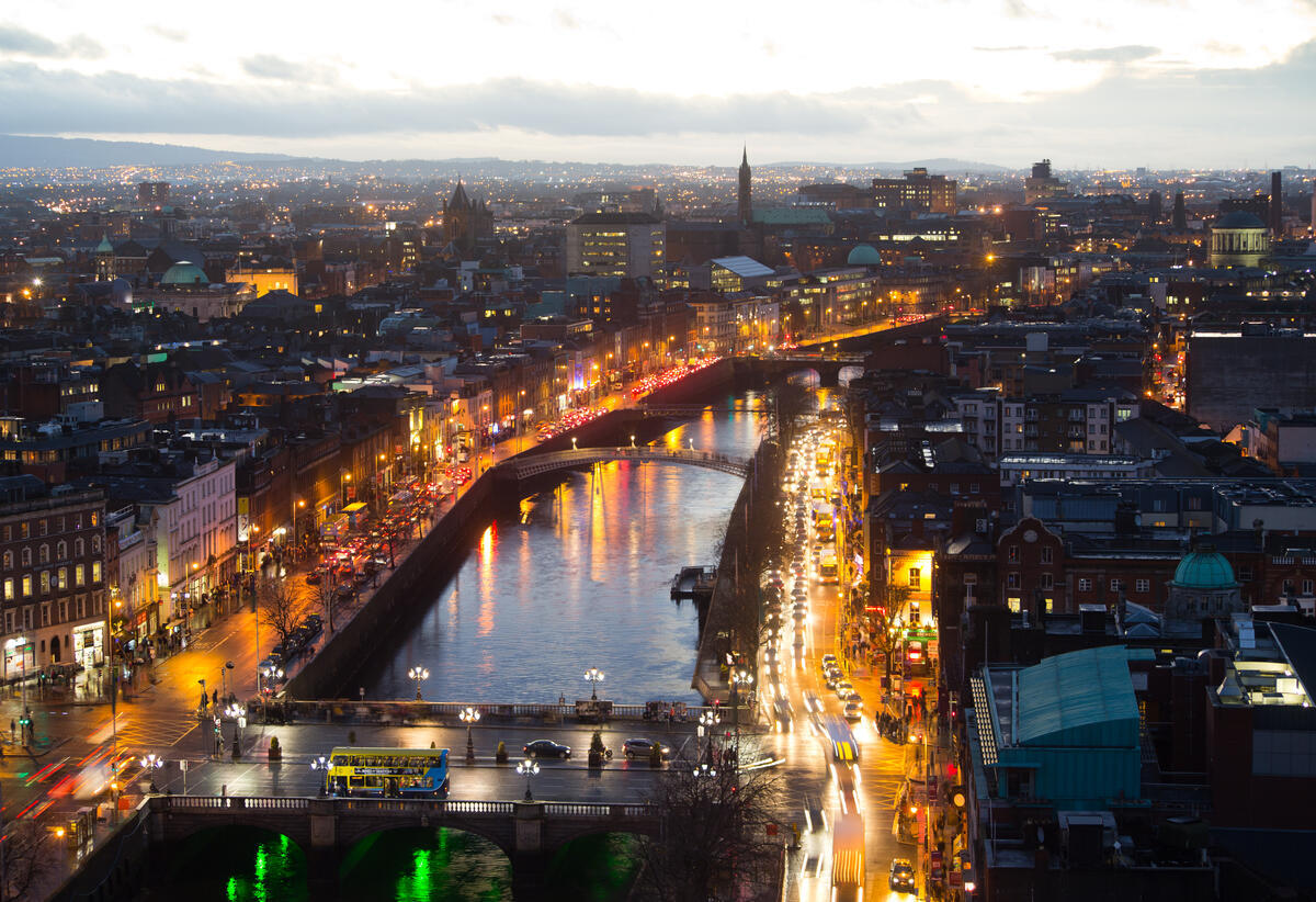 Luftaufnahme des Flusses Liffey bei Nacht - mit Brücken, Verkehr und Lichtern der Stadt; das Stadtzentrum von Dublin und das Custom House sind beleuchtet.
