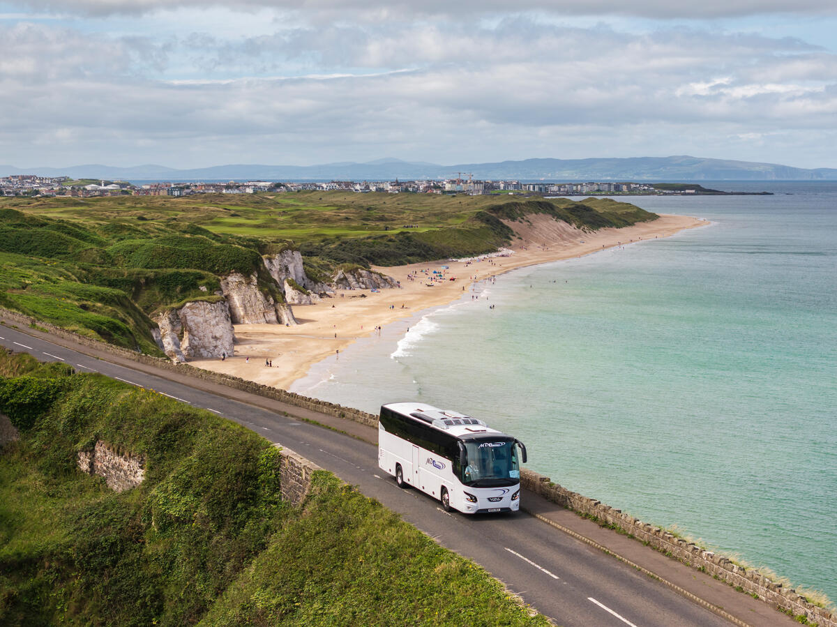 Ein Reisebus fährt entlang der Antrim Coast Road oberhalb eines Sandstrandes nahe Portrush.