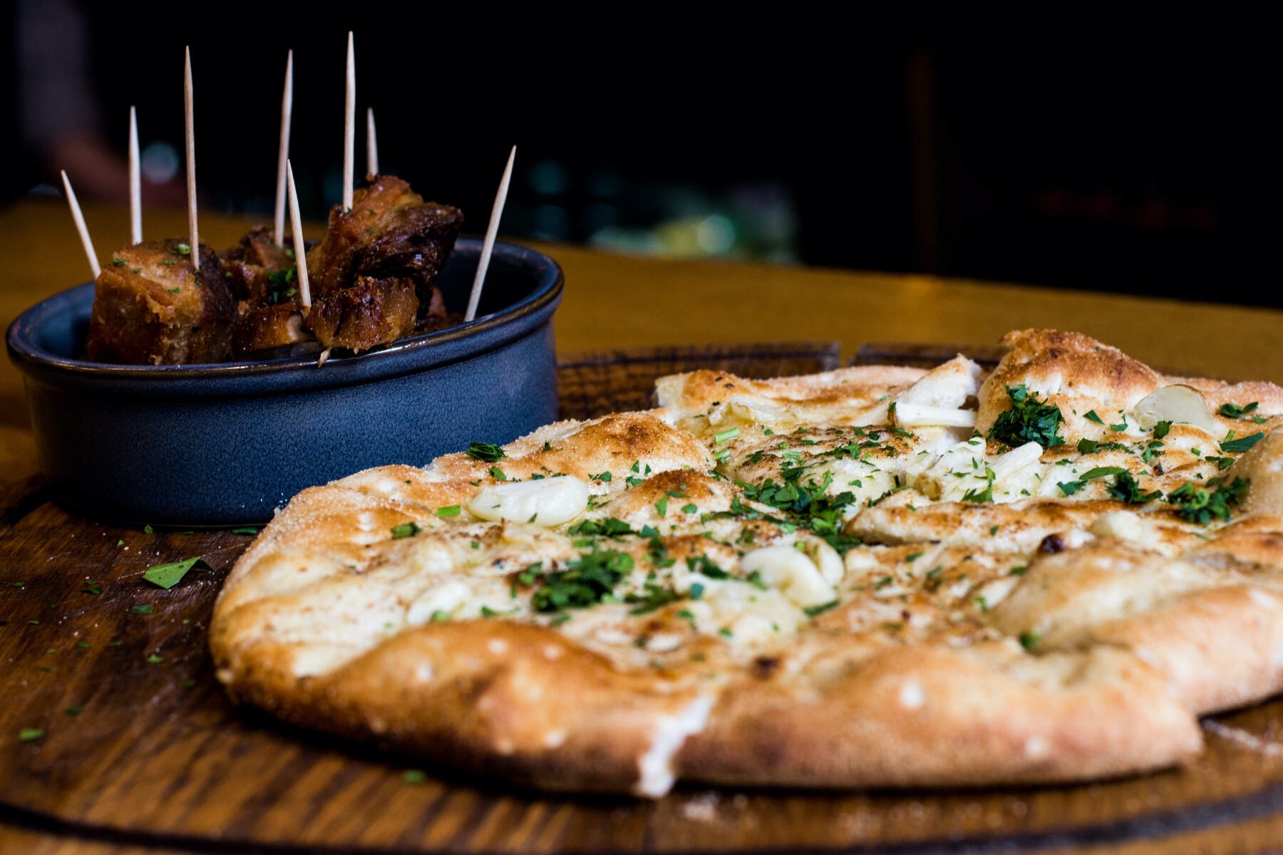 Close-up of flatbread topped with herbs and garlic beside a bowl of skewered meat pieces served at Enniskillen Taste Tour.