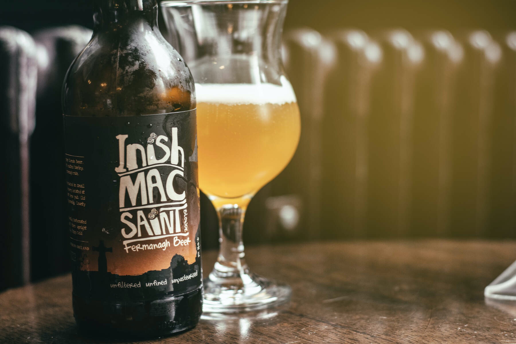 Inish Mac Saint bottle and glass of golden beer on a wooden table showcasing Fermanagh craft brewing.