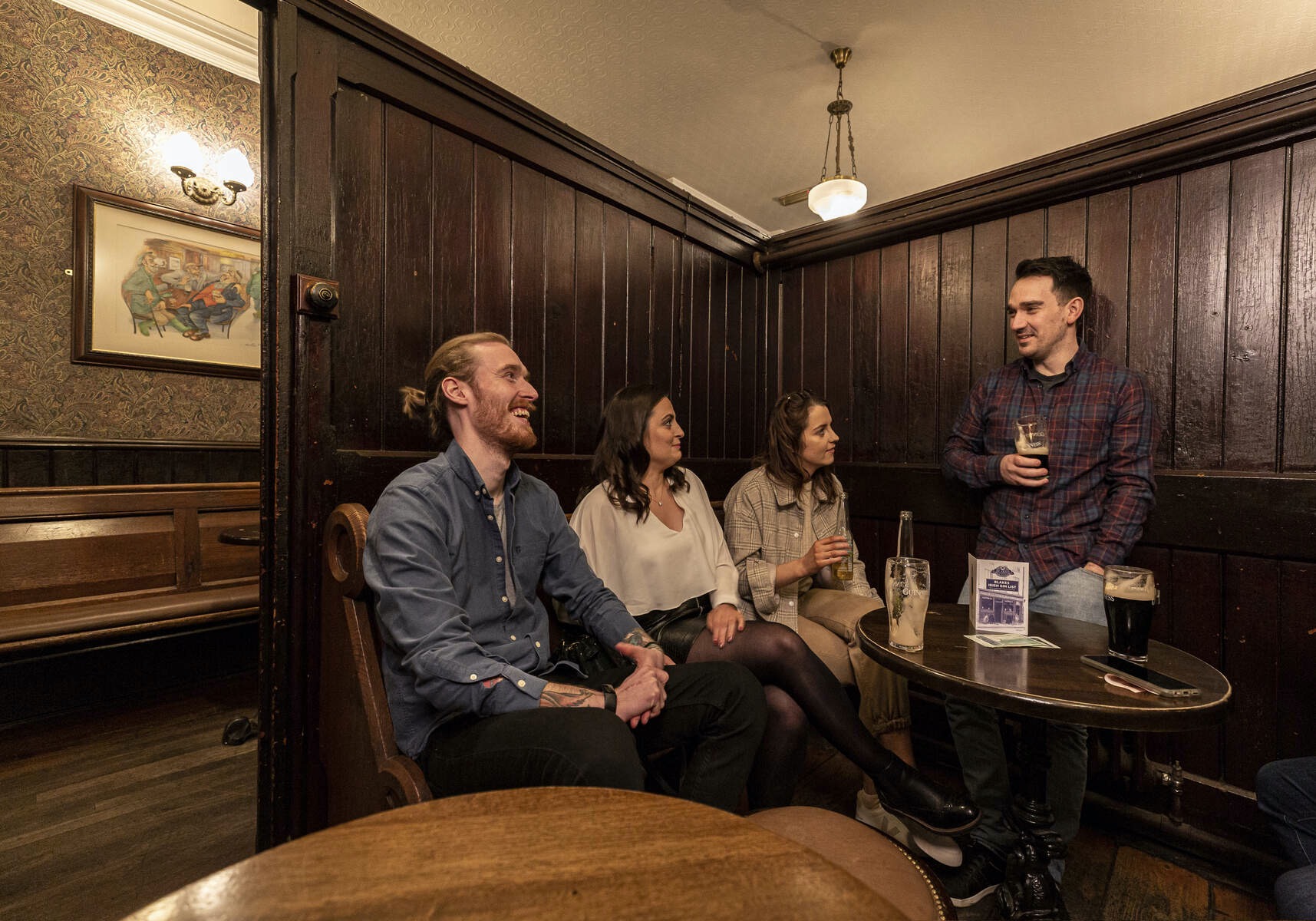 Group of friends laughing and chatting over drinks in the wooden interior of Blakes of the Hollow pub in Enniskillen.
