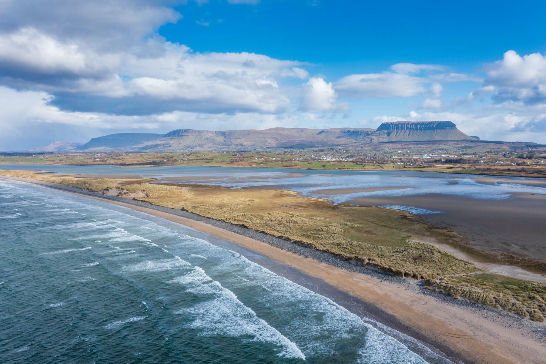 Waves breaking along Strandhill Beach with sandy dunes, tidal flats, and Ben Bulben mountain in the distance.