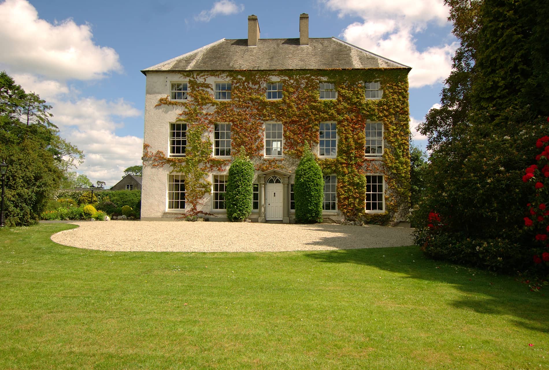 Newforge House in County Armagh, ivy-covered Georgian home with large lawn and blue sky, welcomes guests.