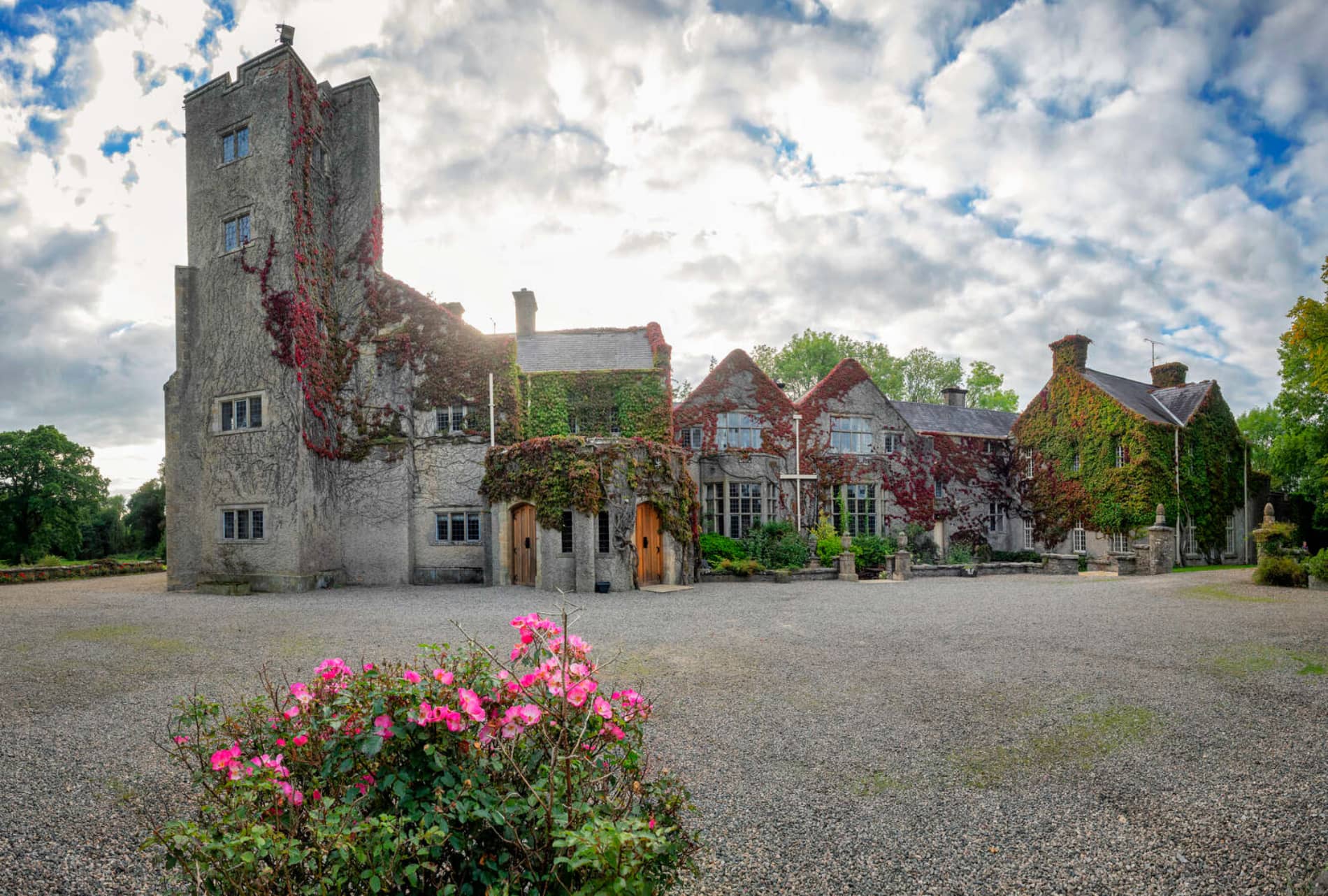 Ivy-covered Belle Isle Castle with tall tower, stone walls, roses, and dramatic cloudy sky.