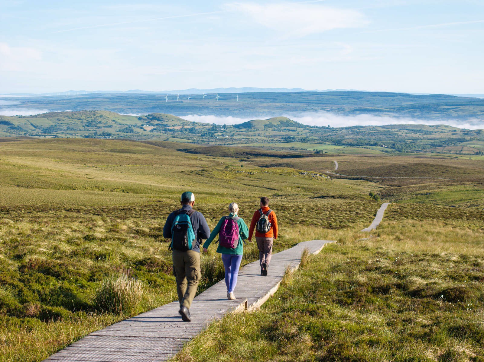 Trois personnes marchent le long du parcours Cuilcagh Boardwalk Trail dans le comté de Fermanagh, avec la zone de tourbière au loin.