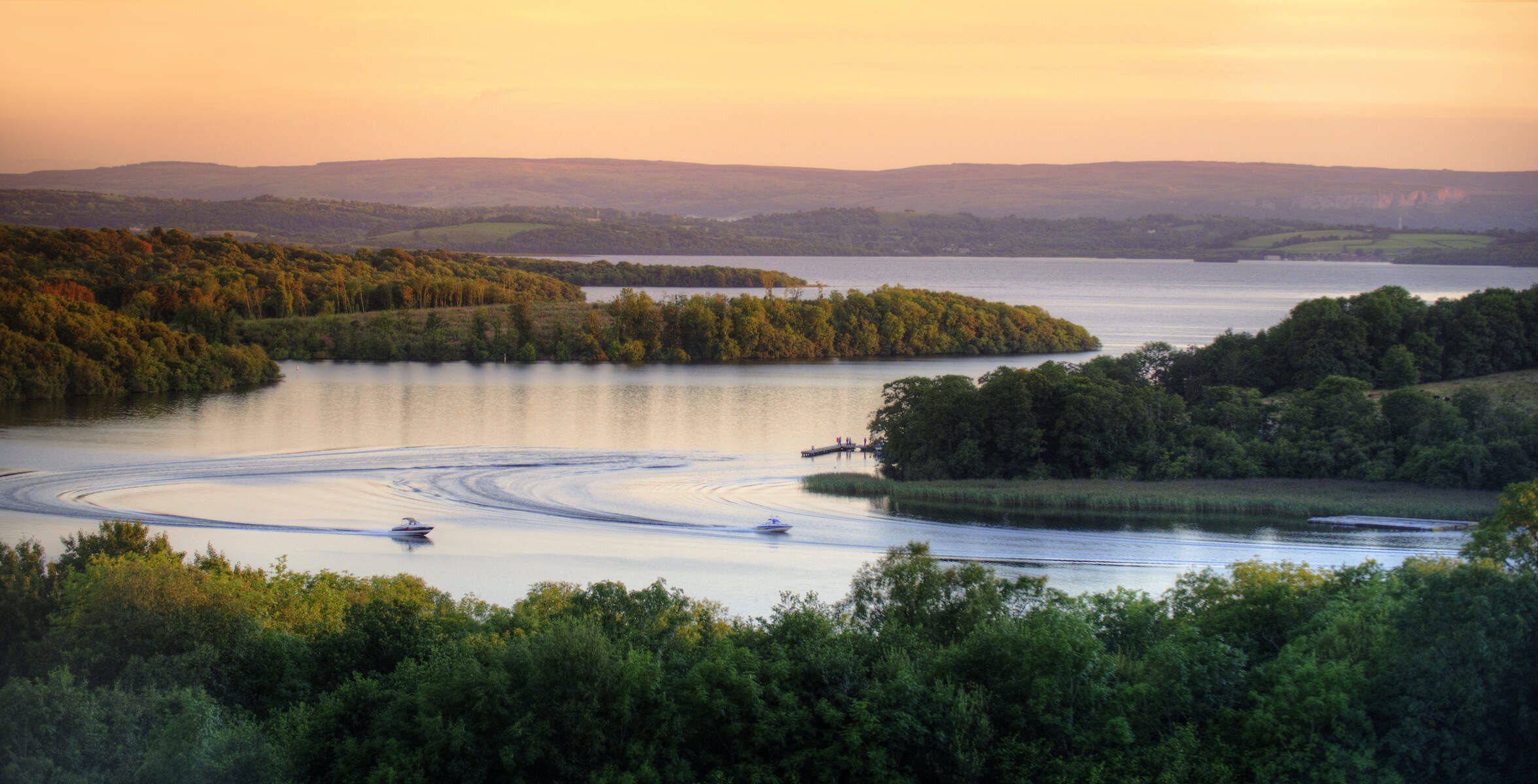 Deux bateaux naviguent dans la paisible région des lacs de Fermanagh au coucher du soleil.