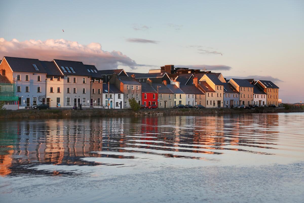 Casas de colores a lo largo de The Claddagh reflejadas en el río Corrib al atardecer en la ciudad de Galway.