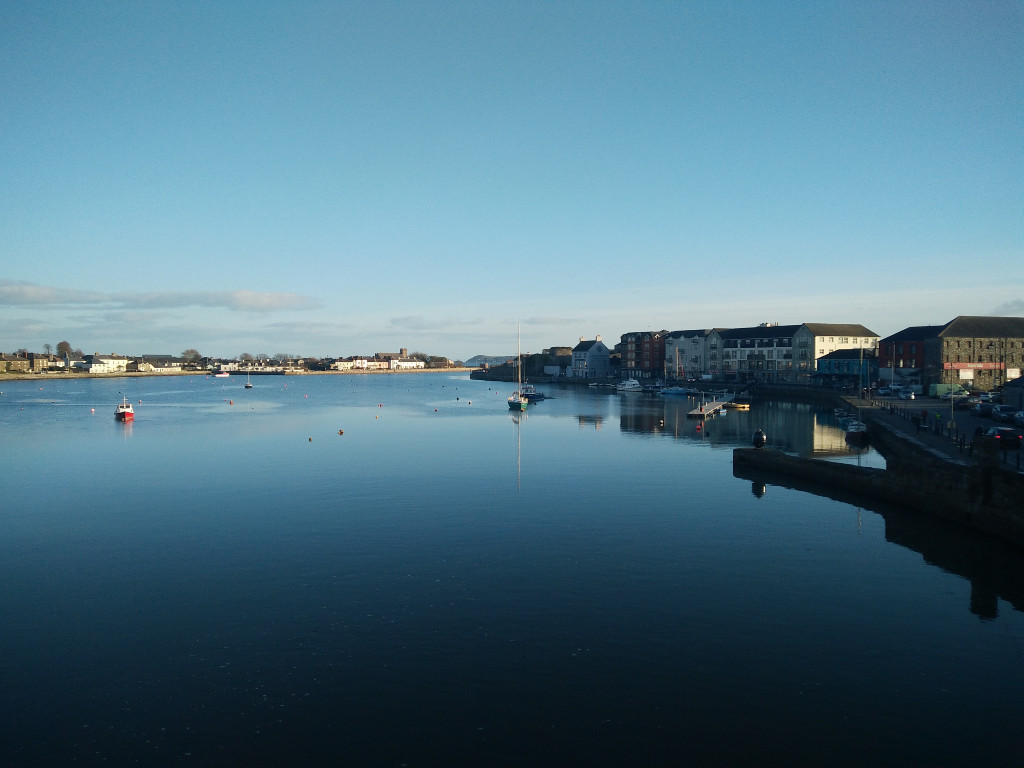 Boats and buildings reflected on the tranquil waters of Dungarvan Harbour, County Waterford under early morning light.
