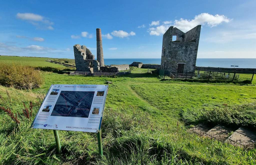 Interpretive panel overlooking 19th-century mine buildings and chimney on Waterford’s Copper Coast.
