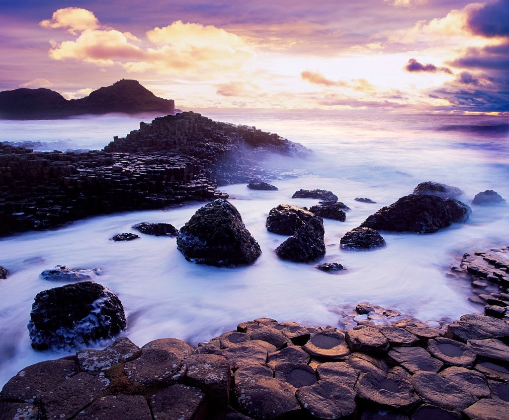 Moody purple skies and sea mist surround the dark basalt columns of the Giant’s Causeway at twilight.