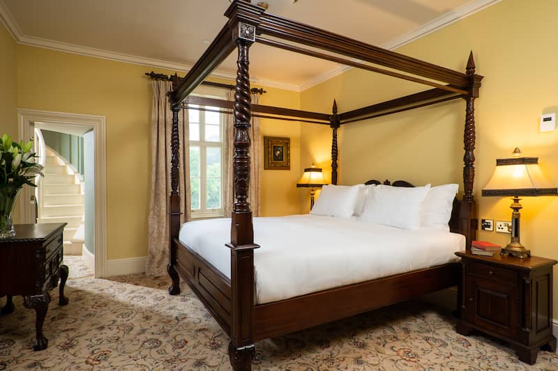 Sunny castle bedroom with white linen on a dark wood four-poster bed and traditional décor throughout.