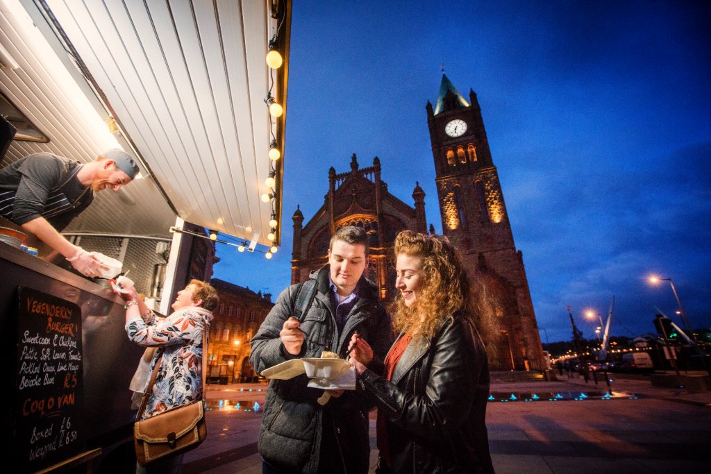 Stand de street food la nuit à Derry~Londonderry, avec des personnes dégustant des plats à emporter devant le Guildhall.