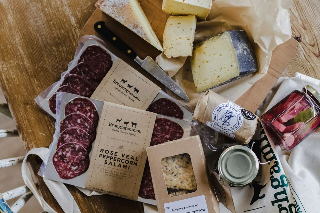 Sélection de produits artisanaux de Broughgammon, dans le comté d’Antrim, avec salami, fromages et conserves sur une table rustique.