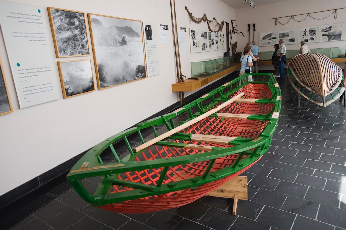 Traditional boats on display inside the Blasket Island Centre, with visitors viewing maritime exhibits and historic photos.