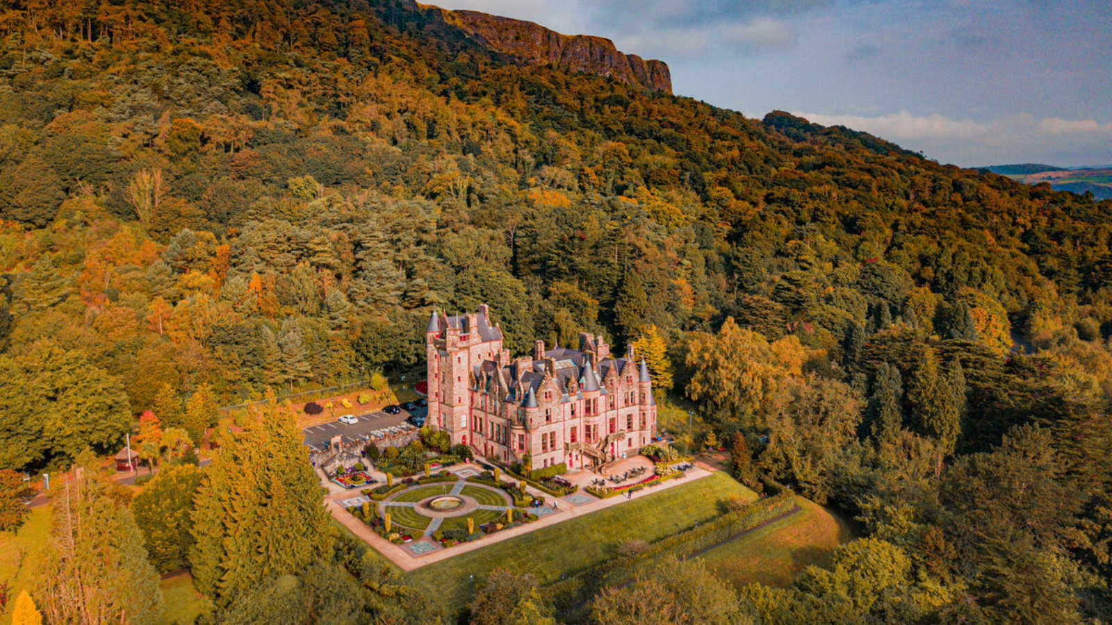 Belfast Castle liegt inmitten des Herbstwaldes auf den Hängen des Cave Hill und leuchtet im warmen Sonnenlicht über der Landschaft von Belfast.
