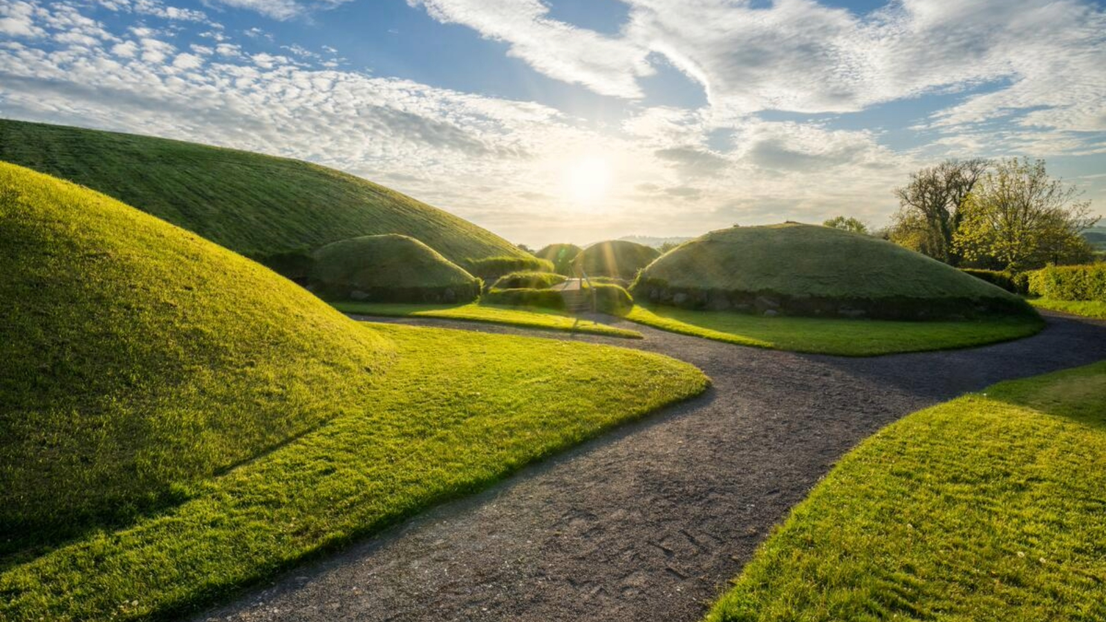 Path between grass-covered passage tomb mounds at Knowth, County Meath, in warm evening light.