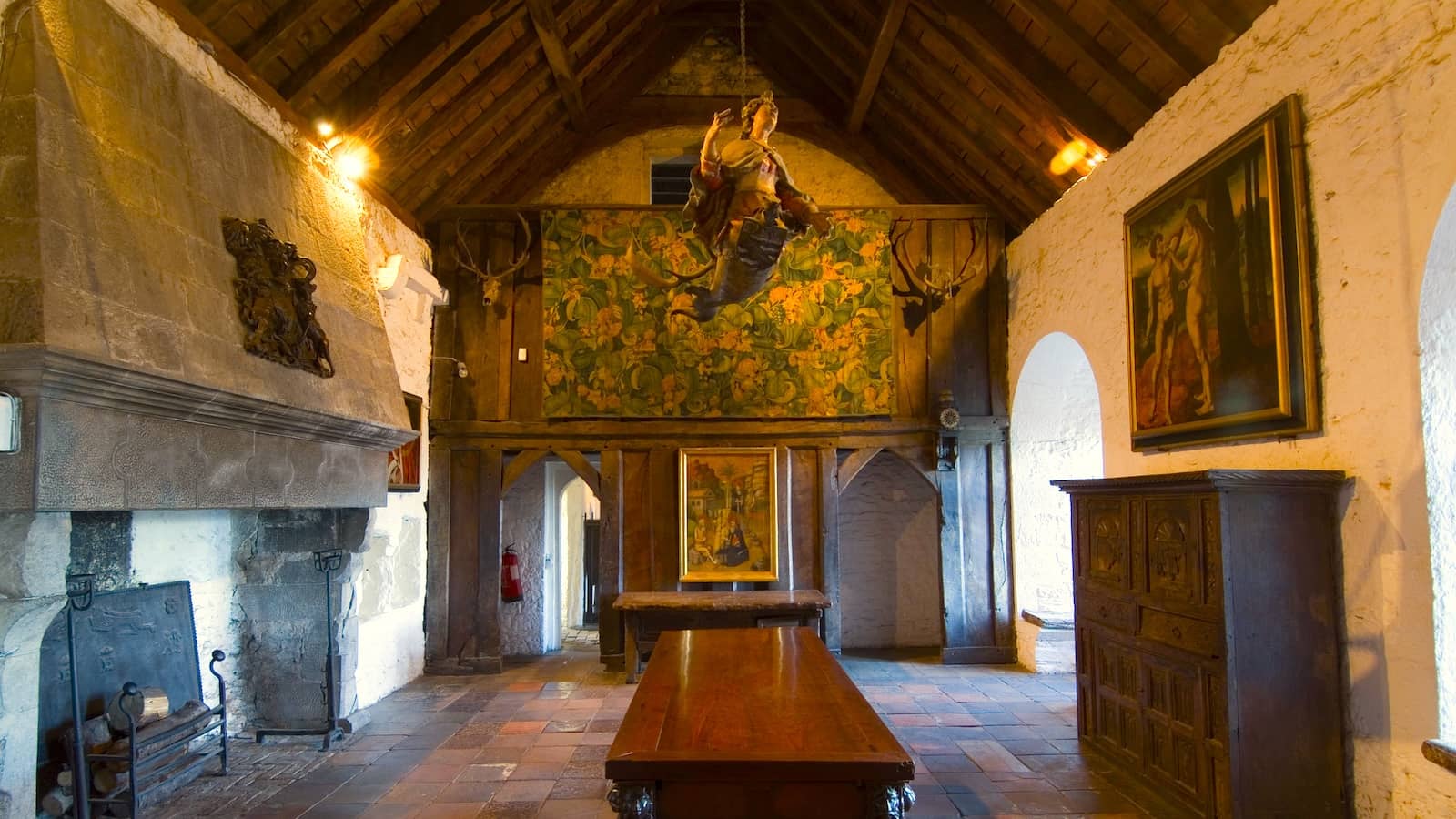Interior of Bunratty Castle’s Great Hall, featuring a long wooden table, stone fireplace and medieval artwork.