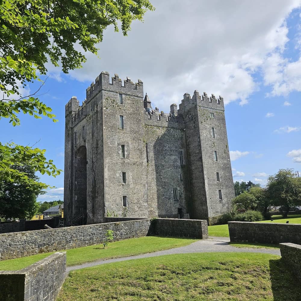 Bunratty Castle in County Clare, surrounded by green lawns and trees under a blue sky.