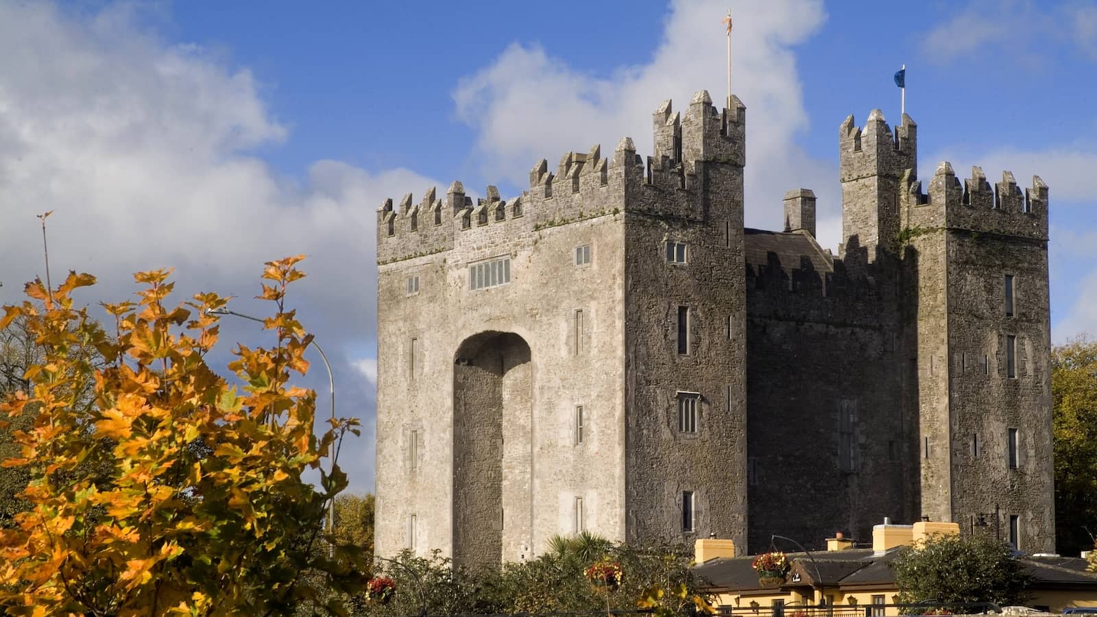 Bunratty Castle framed by autumn foliage, its stone towers rising above colourful leaves under a bright sky.