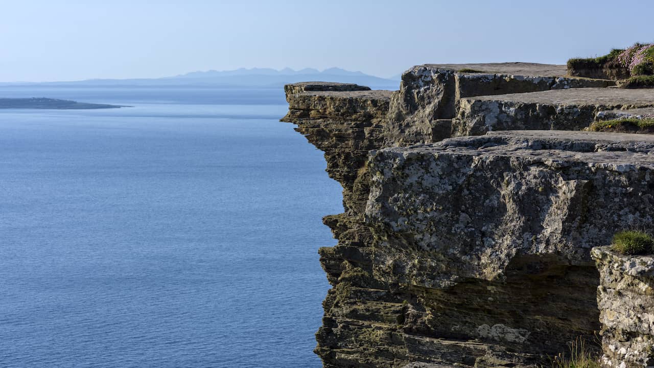 Cliffs of Moher overlooking the Atlantic Ocean with rugged limestone cliffs under a clear blue sky.