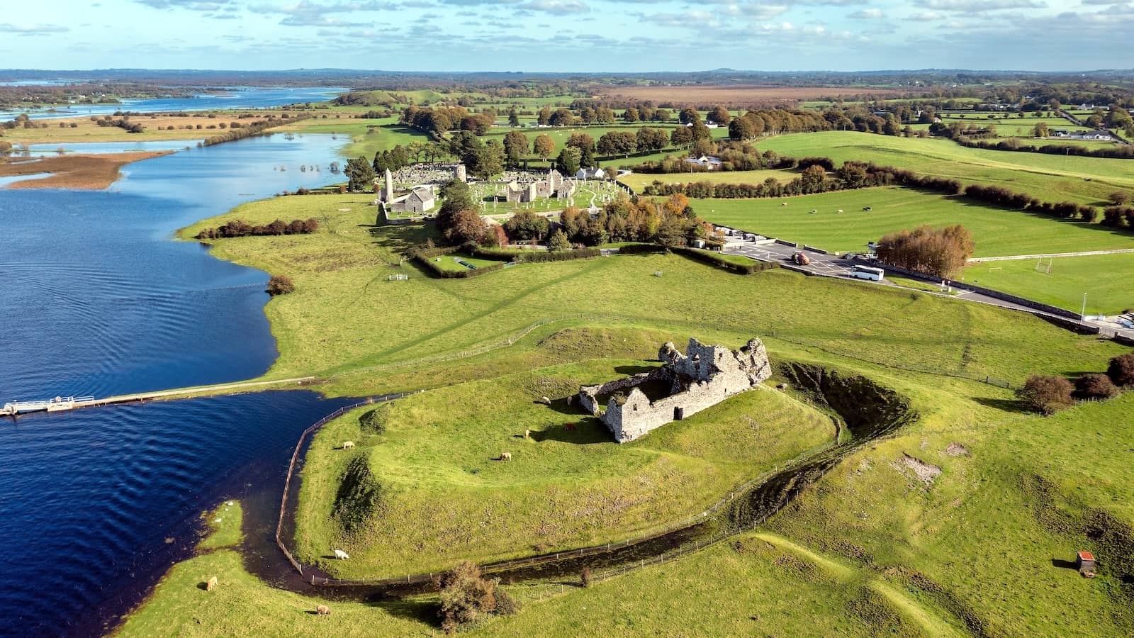 Luchtfoto van de kloosternederzetting Clonmacnoise aan de rivier Shannon, omgeven door groene velden in county Offaly.