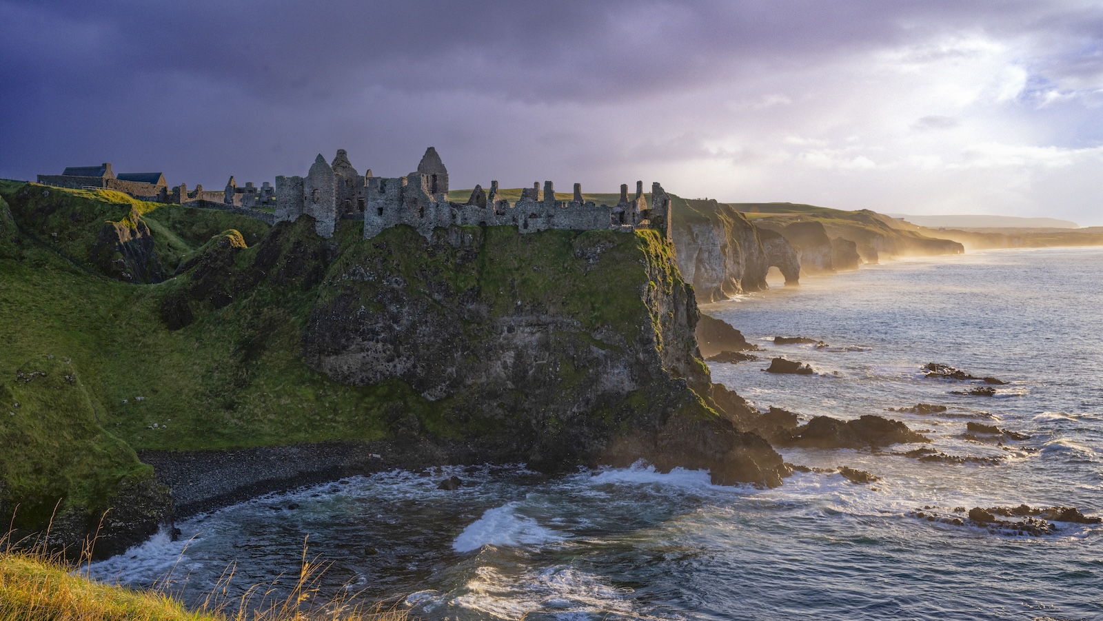 Le rovine del castello di Dunluce arroccate su spettacolari scogliere lungo la Causeway Coast al tramonto.