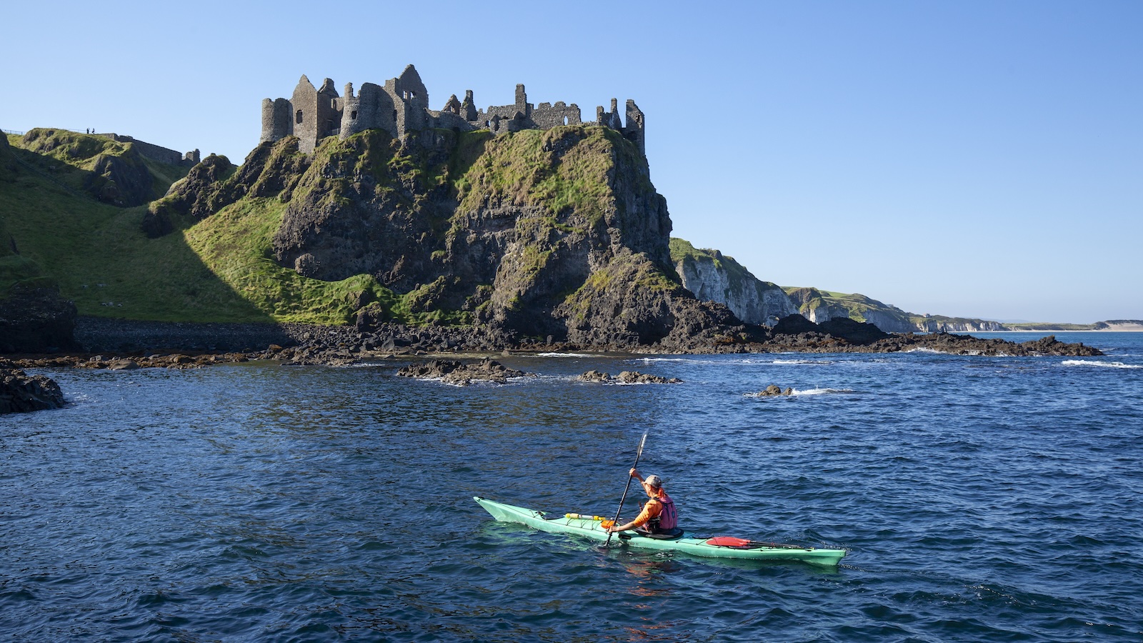 Kayakista che pagaia sotto il castello di Dunluce sulla Causeway Coast.