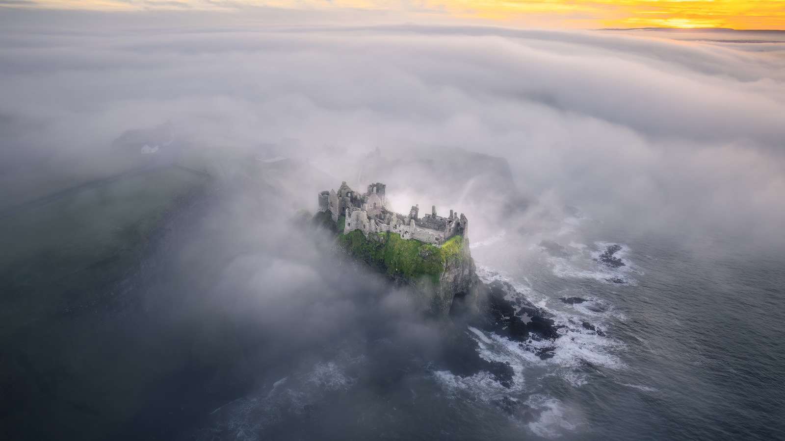 Vista aerea del castello di Dunluce che appare dalla nebbia marina sopra l'Oceano Atlantico.