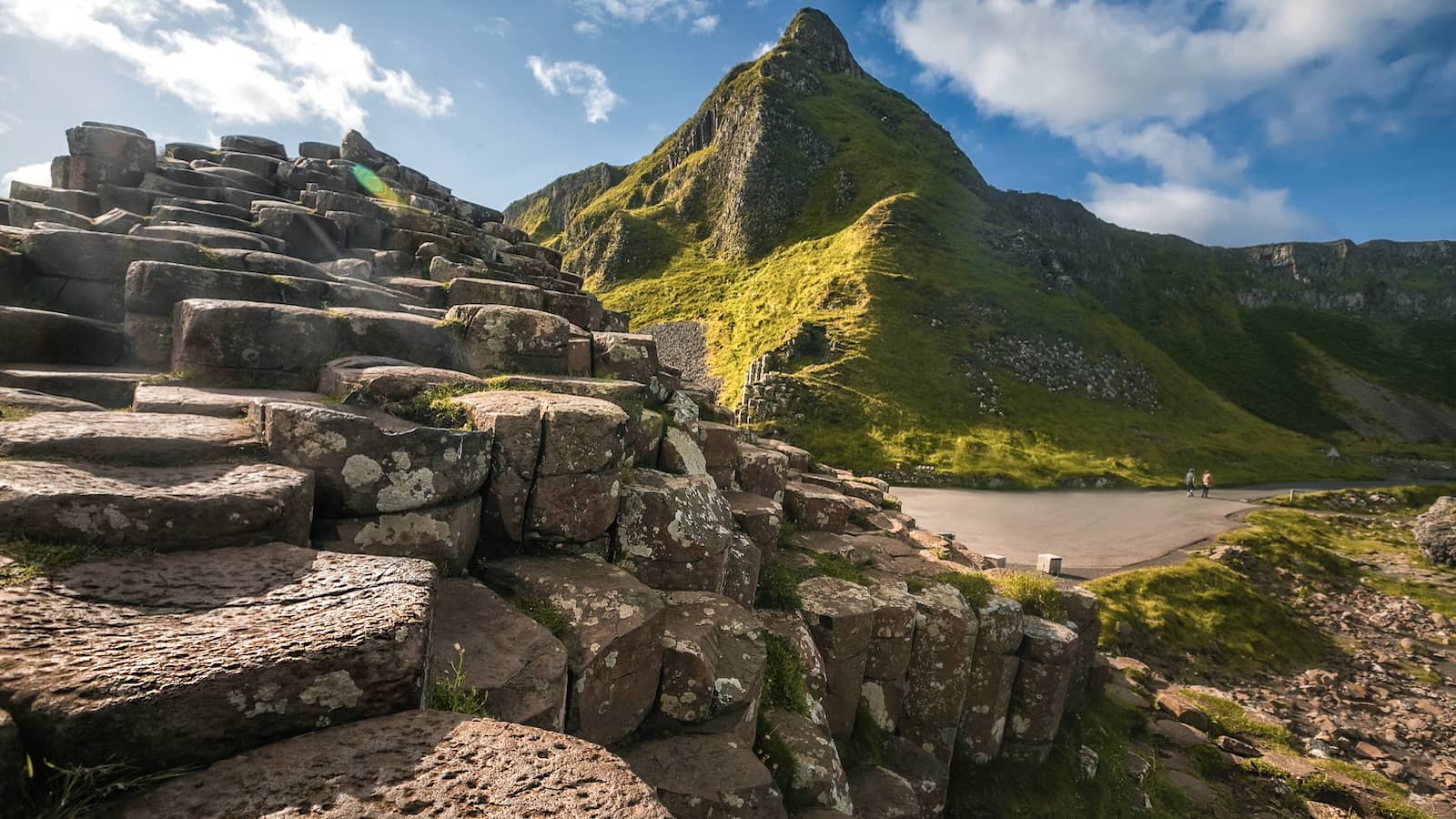 Weathered basalt columns at the Giant’s Causeway set against steep green cliffs under bright skies.