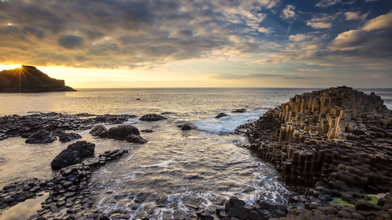 Sunset over the Giant’s Causeway with hexagonal basalt columns and waves along the rugged Antrim coast.