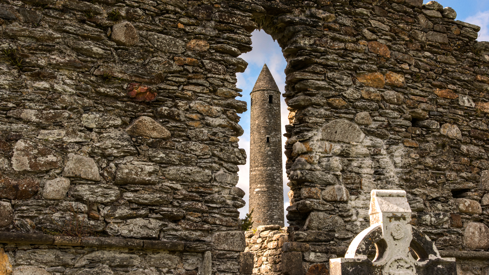 Glendalough round tower framed by the stone arch of a ruined monastic building.