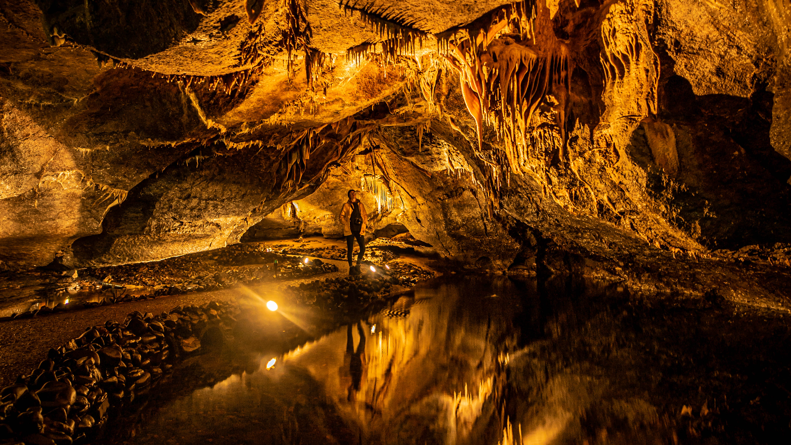 Mitten in den Marble Arch Caves steht ein Besucher, umgeben von beleuchteten Stalaktiten und glitzernden unterirdischen Wasserbecken in der Grafschaft Fermanagh.