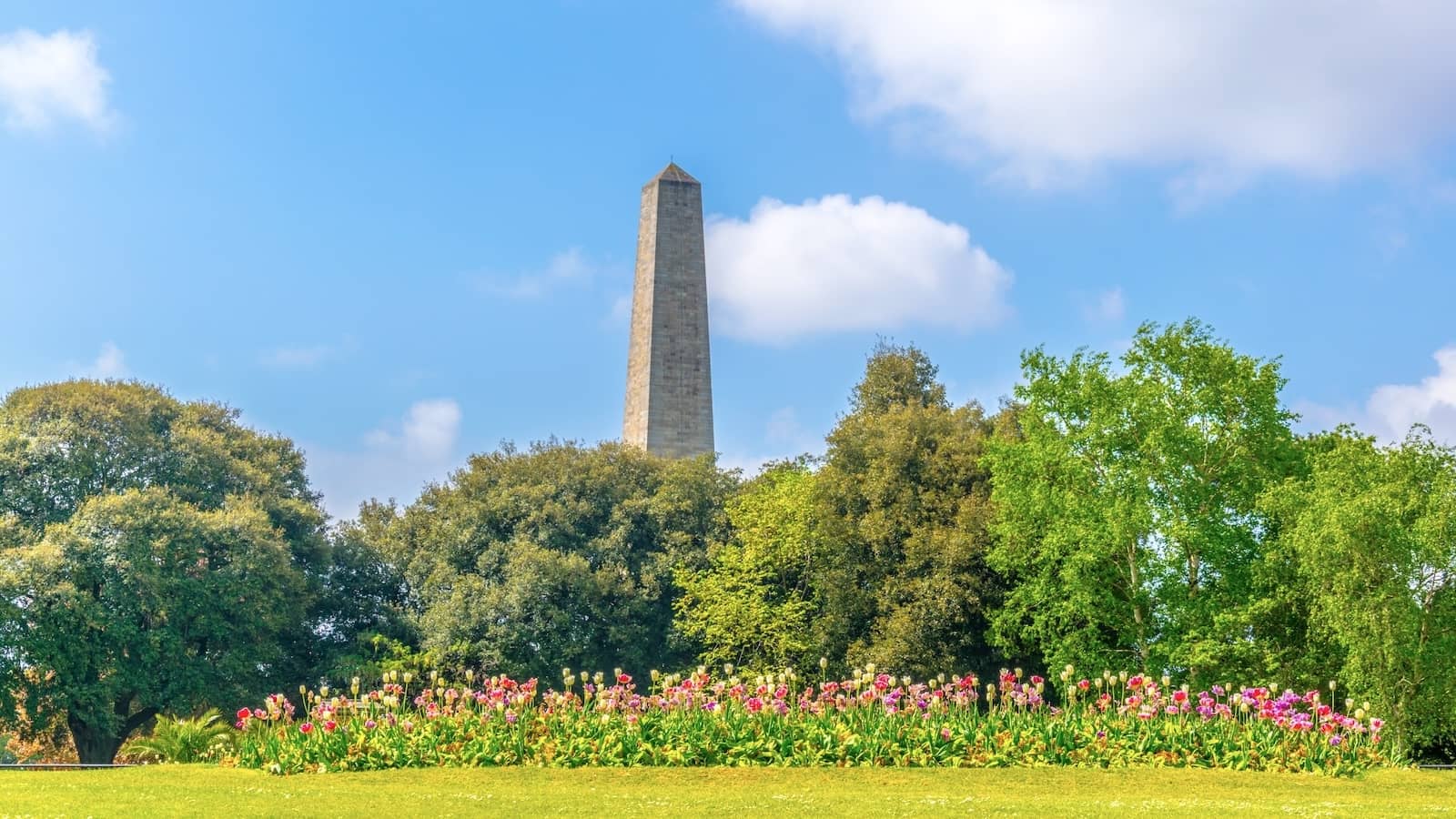 Wellington Monument rising above trees and colourful flowerbeds in Phoenix Park, Dublin.