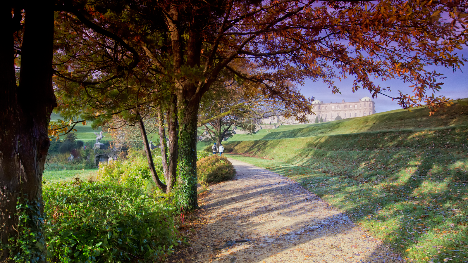 Autumn pathway in Powerscourt Gardens with trees framing Powerscourt House on the hill in County Wicklow.