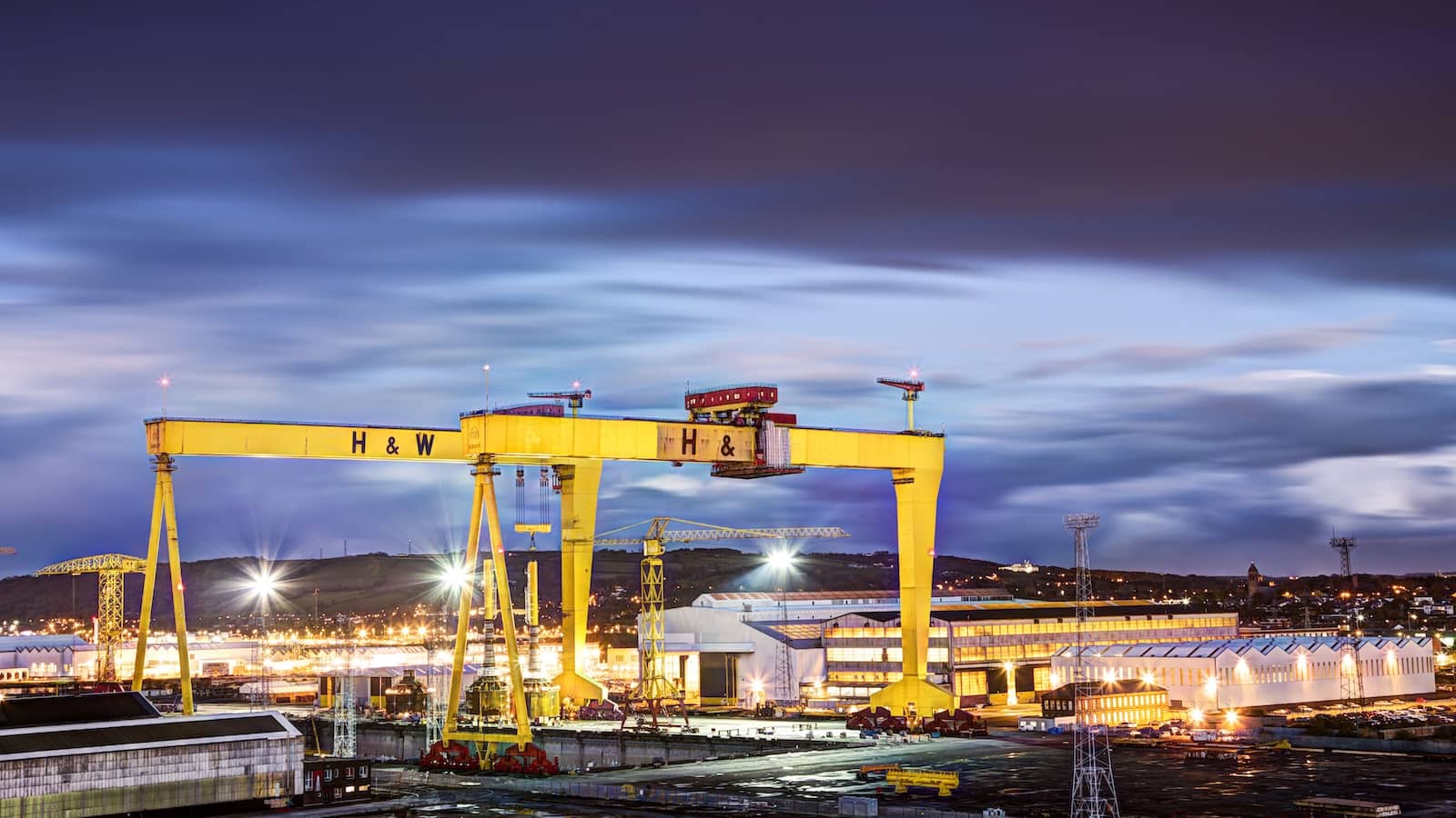 Die legendären gelben Werftkräne von Harland & Wolff, die vor dem tiefblauen Abendhimmel in Belfast erleuchten.